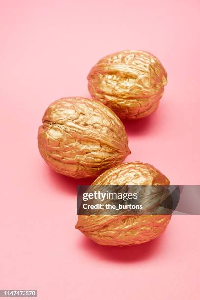 still life of three golden walnuts on pink background - walnuts stockfoto's en -beelden