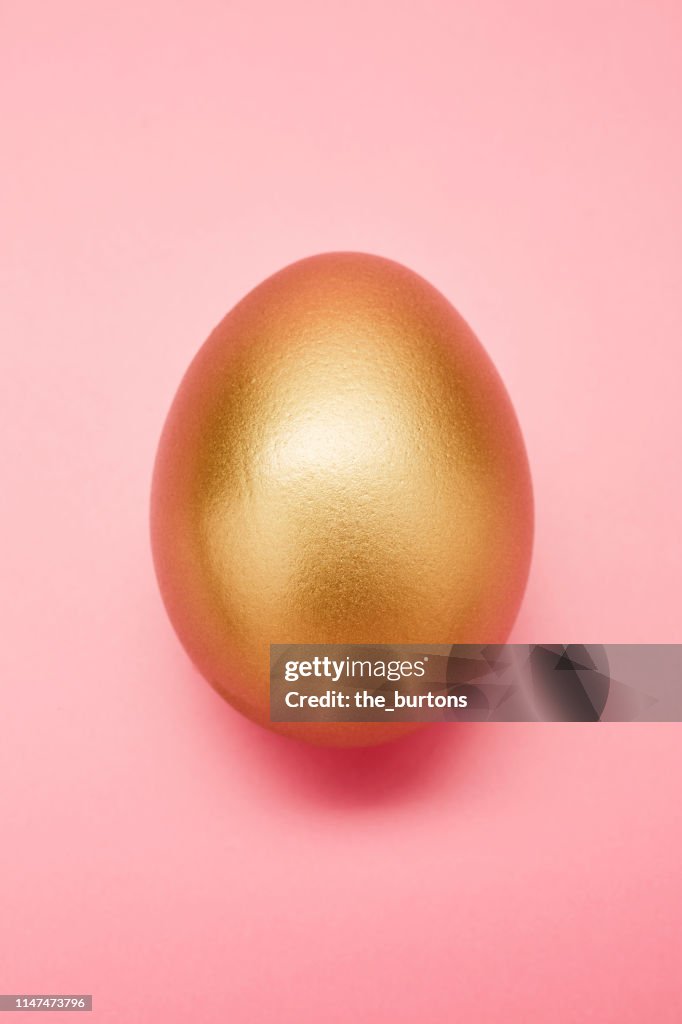 Still life of a golden egg on pink background
