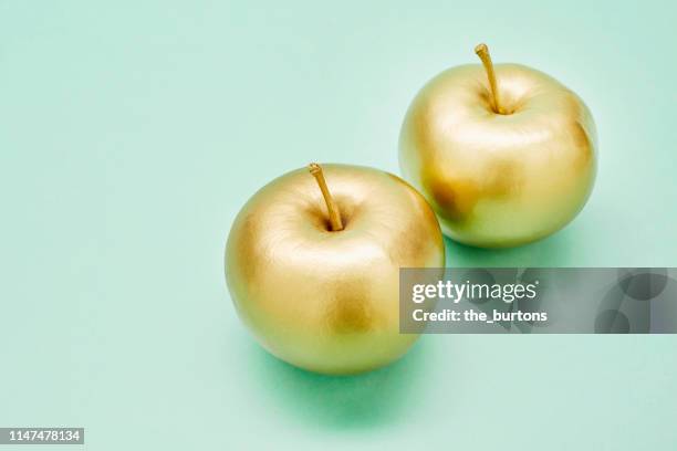 still life of two golden apples on turquoise background - gold number 2 stock pictures, royalty-free photos & images