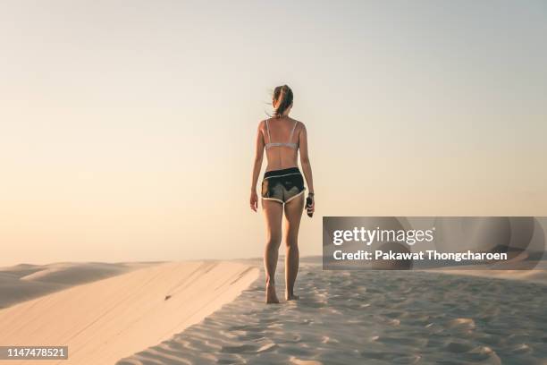 young asian woman in bikini top walking at the edge of sand dune at sunset, lencois maranhenses, brazil - barreirinhas stock pictures, royalty-free photos & images