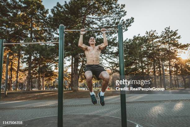 handsome young athlete doing chin-ups on horizontal bar - horizontal bar stock pictures, royalty-free photos & images