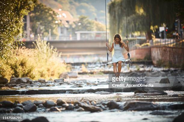 young woman swings over stream - freiburg im breisgau stock pictures, royalty-free photos & images