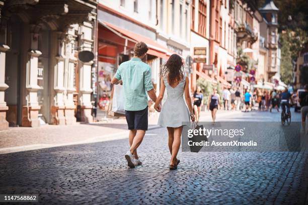 couple walk down promenade with shopping bags - blue shirt back stock pictures, royalty-free photos & images