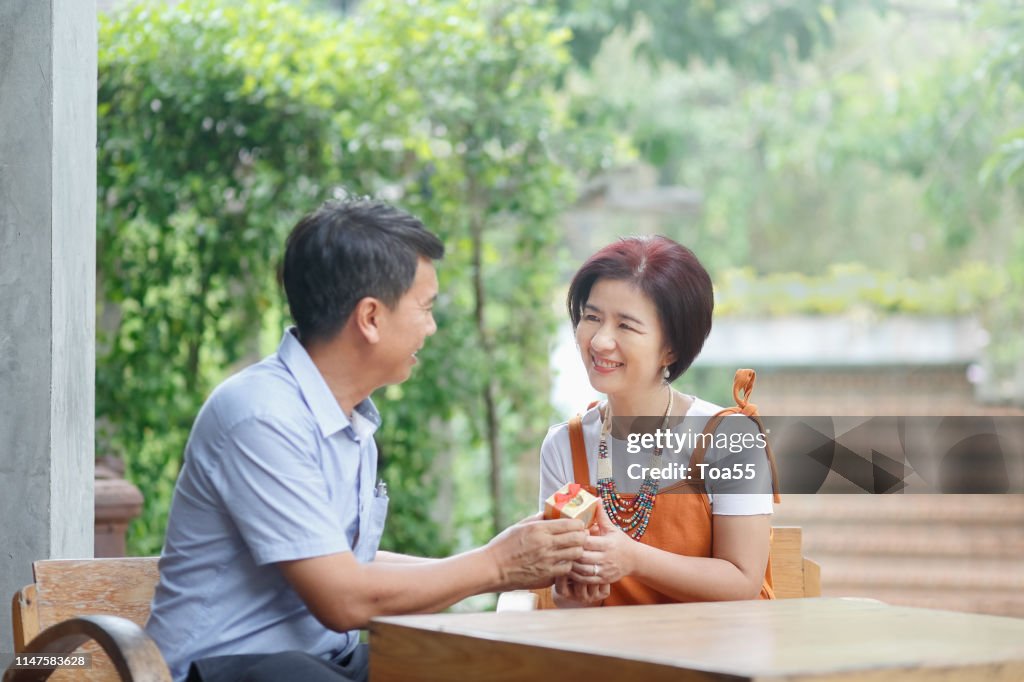 Aziatische man van middelbare leeftijd geeft een cadeautje aan zijn vrouw in verjaardag trouwdag