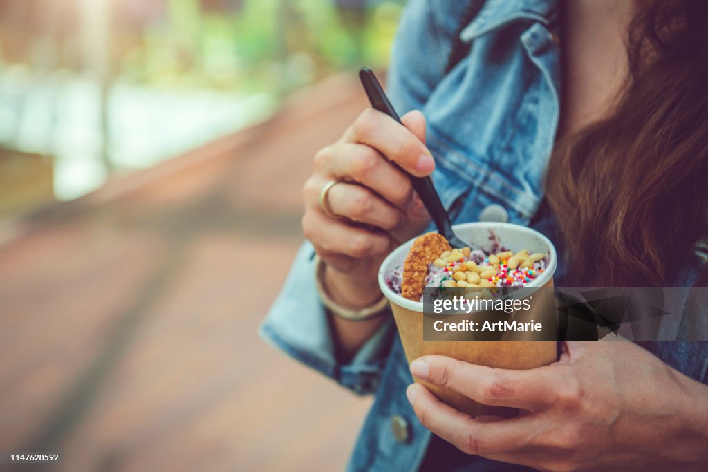 Young woman eating healthy rolled ice-cream or yogurt with fruits or berries, cookies, candy and mint