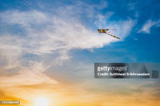 low angle view of colorful kite flying against blue sky  during sunset - kite flying stock pictures, royalty-free photos & images