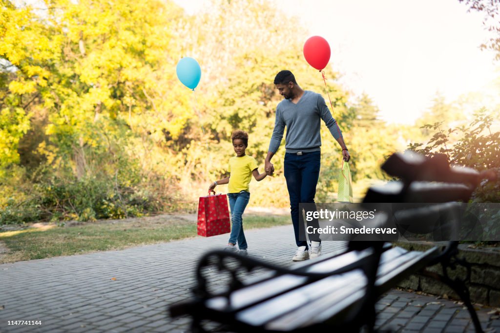 Father and daughter walking in the park after shopping holding hands together.