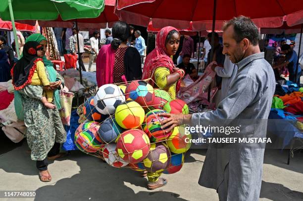 An Indian street vendor looks on carrying a net of footballs as a customer looks at them at a market ahead of the Muslim festival of Eid al-Fitr in...