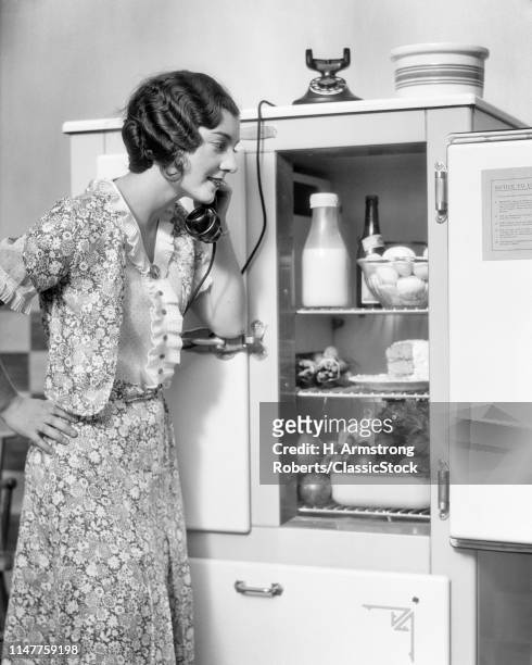1920s SMILING WOMAN SPEAKING ON TELEPHONE LOOKING INTO THE KITCHEN ICEBOX REFRIGERATOR PLACING ORDER WITH GROCER