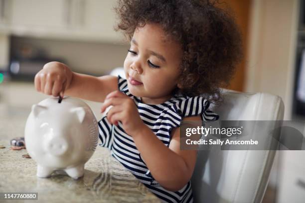child putting coins into a piggy bank - kids money fotografías e imágenes de stock