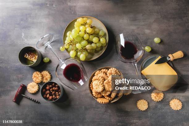 Wine snack. Cheese, grapes, nuts, cheese crackers cookies, honeycombs with laying glass of red wine and knife over dark texture background. Flat lay,...