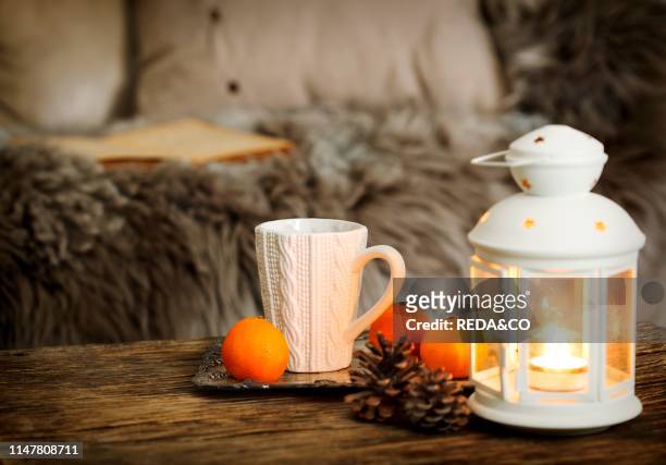 Cup of tea and candles on wooden table near the sofa with pillows.
