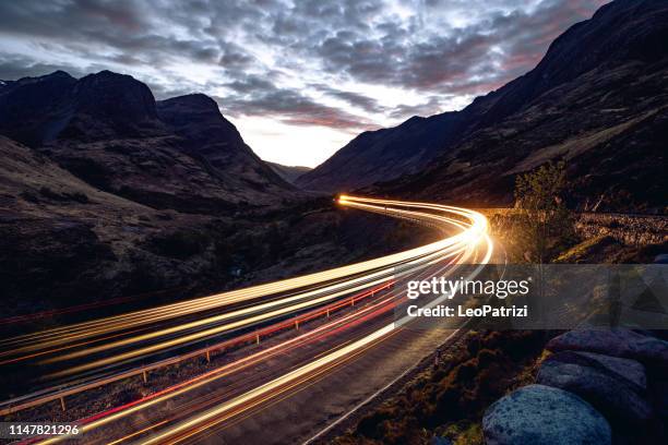 light trails in the night on a remote road in mountains - car night stock pictures, royalty-free photos & images