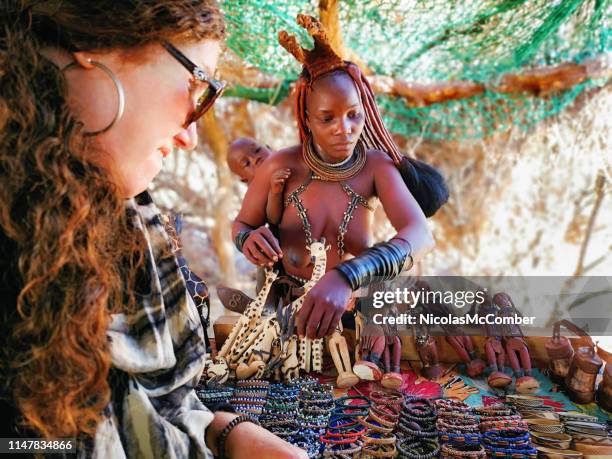 junge himba-frau verkauft armbänder an einen touristen am dorfmarkt - africa craft stock-fotos und bilder