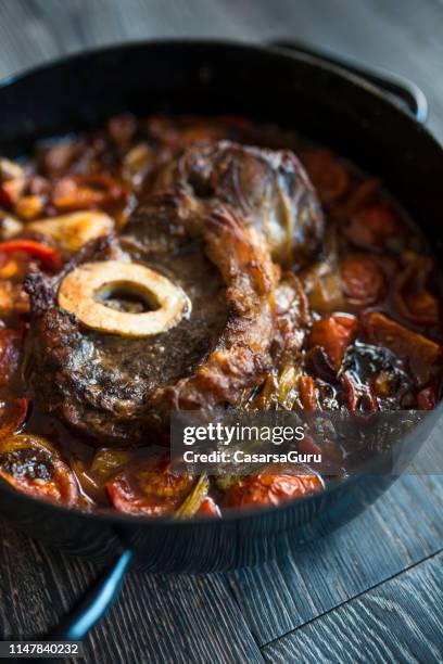 gekochte osso-keufterschenkel mit gemüse im gießeisernen topf auf holzrücken - osso bucco stock-fotos und bilder