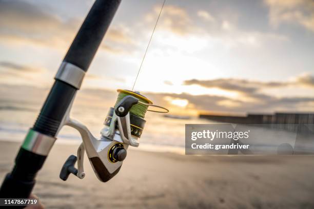 a close-up view of a fishing pole with the beach and waves at sunset near the international border wall  in playas tijuana, mexico - fishing reel stock pictures, royalty-free photos & images