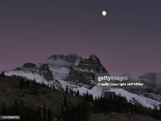 granite park chalet beneath moon and snow capped mountains at dusk, glacier national park, montana, usa. - kalispell montana stockfoto's en -beelden