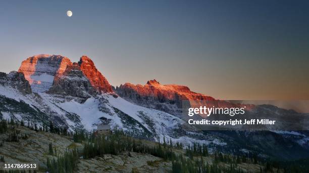 granite park chalet beneath snow capped mountains and rising moon at sunset, glacier national park, montana, usa. - american wilderness stock pictures, royalty-free photos & images