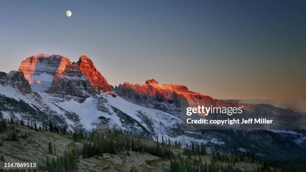 granite park chalet beneath snow capped mountains and rising moon at sunset, glacier national park, montana, usa. - montana mountains imagens e fotografias de stock