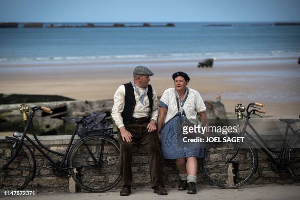 Two person dressed as local resident during the WWII sits on a wall along the beach in Arromanches-Les-Bains, on June 3 ahead of ceremonies marking...