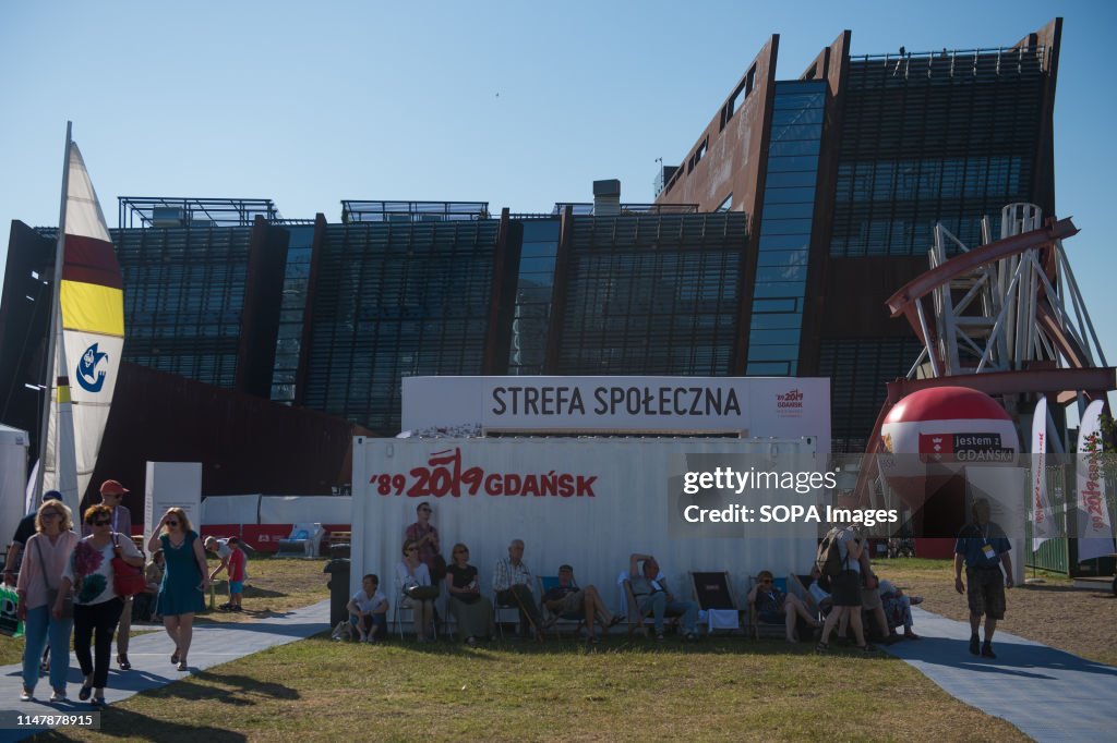 People sit next to a container with the logo of the 30th...