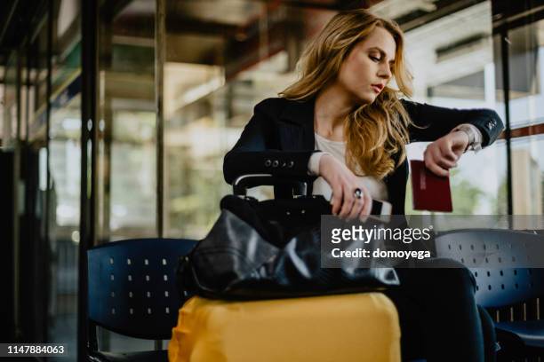 giovane donna che controlla l'ora e aspetta in aeroporto - waiting foto e immagini stock