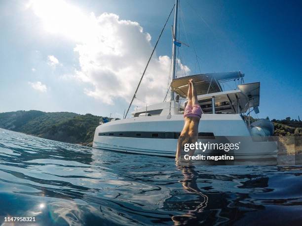 young man jumping down from the white catamaran into the blue water of the ionic sea - 1m diving stockfoto's en -beelden