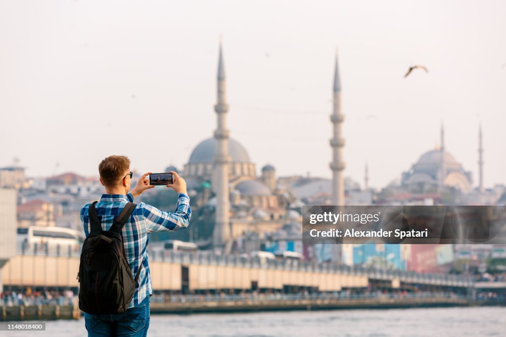 Tourist photographing Istanbul skyline with smart phone, rear view