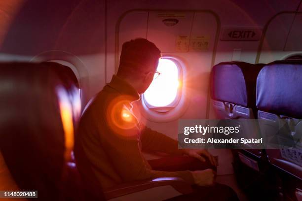 young man looking out of the window in flying airplane during sunset - airplane window stockfoto's en -beelden