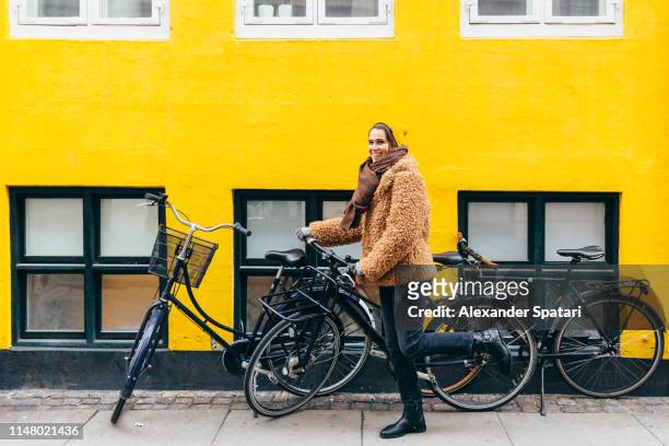 Happy young smiling woman with bicycle against yellow wall in Copenhagen
