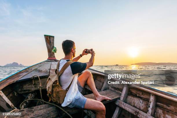 young man photographing sunset while sailing on a long-tail boat in thailand - male photographer stock pictures, royalty-free photos & images