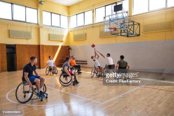 atleta adaptativo en una silla de ruedas que toma un tiro en una cancha de baloncesto - baloncesto en silla de ruedas fotografías e imágenes de stock