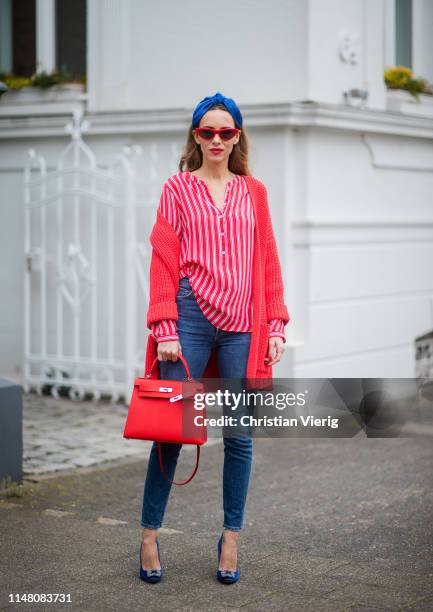 Alexandra Lapp is seen wearing a red chunky knit cardigan styled over a red-white-striped blouse and blue jeans - all from Brax, red cat-eye...