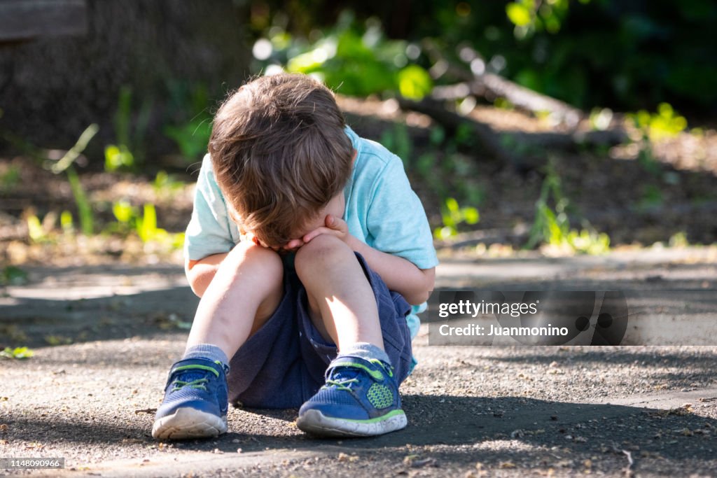 Weinendes Kleinkind, das auf dem Boden sitzt und sein Gesicht bedeckt