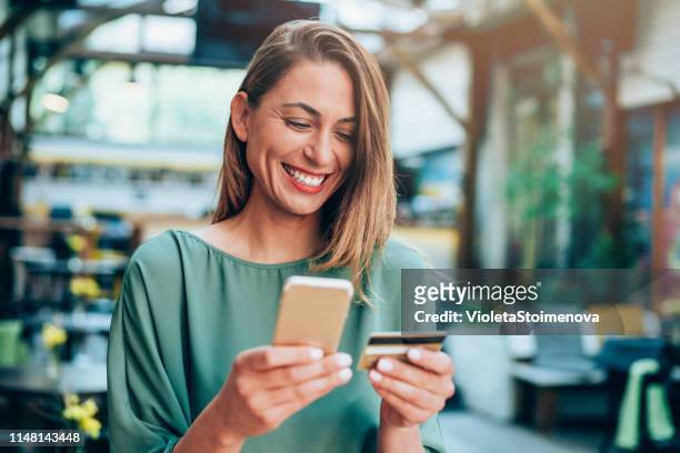 chica sosteniendo tarjeta de crédito y enviando mensajes de texto - compra por tarjeta de crédito fotografías e imágenes de stock