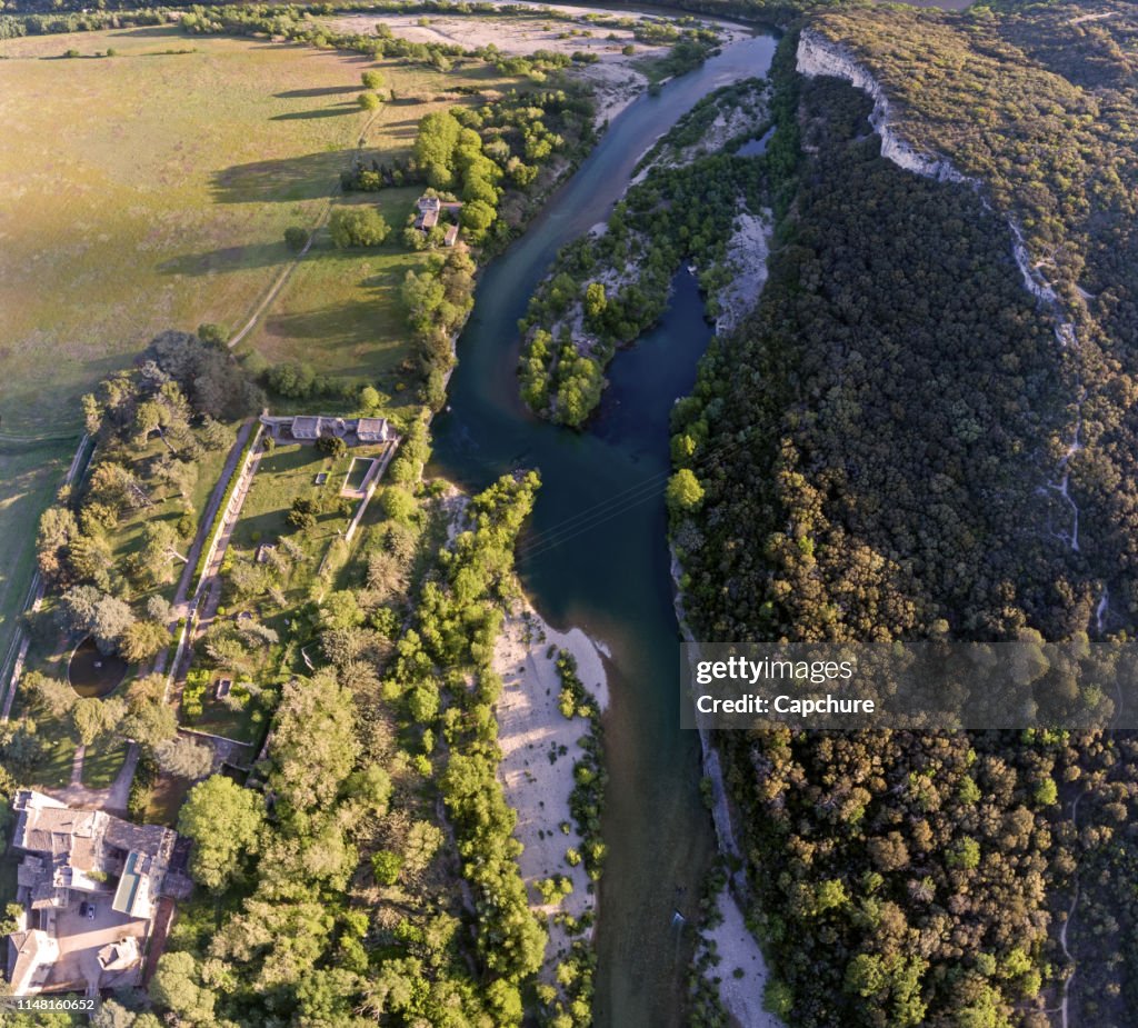 Stunning aerial drone shot of the Rhone river at sunrise. The river reflects the early morning sun and the river gorge is forested and green.