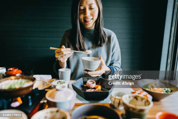 smiling young asian woman enjoying delicate japanese style cuisine with various side dishes, seafood and green tea in restaurant - woman sushi stock-fotos und bilder