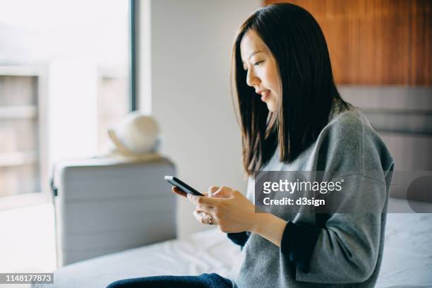 young female traveller using smartphone in hotel room while on vacation - women reservation stock pictures, royalty-free photos & images