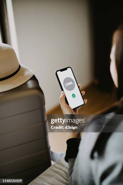 young female traveller lying on bed making hotel reservations on smartphone in hotel room while on vacation - facebook check in stock pictures, royalty-free photos & images