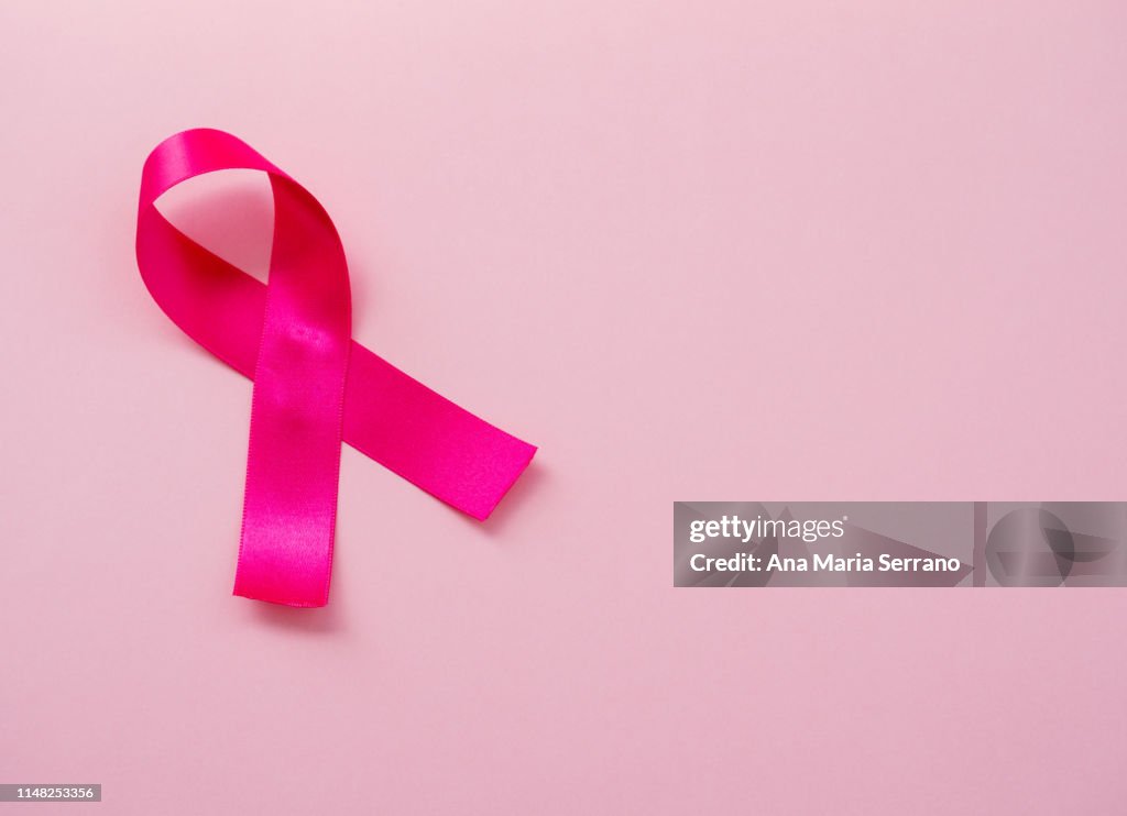 A pink ribbon on a pastel pink background. Breast cancer concept