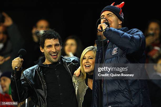 Olivia Newton John performs with Russell Robertson and Jim Stynes the president of the Demons before the round 10 AFL match between the Melbourne...