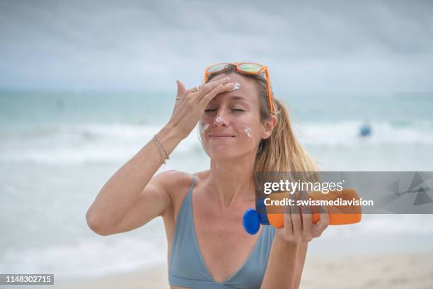 summertime - young woman on beach applying sunscreen on her face, protection on skin - sunscreen imagens e fotografias de stock