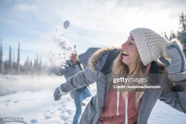 playful young couple throwing snowballs at each other at sunset having fun and enjoying winter vacations - snowball stock pictures, royalty-free photos & images