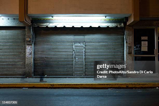 store front with locked roll-up door at night - cerrado imagens e fotografias de stock