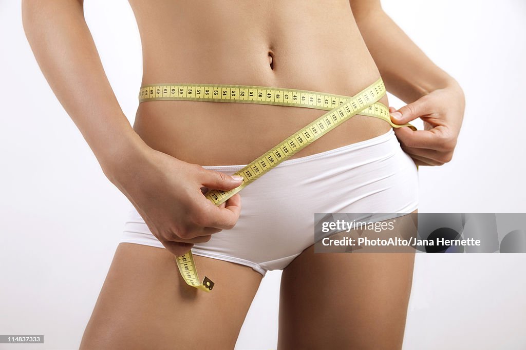 Young woman measuring hips with measuring tape, cropped