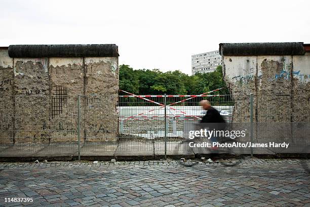 germany, berlin, person bicycling past dismantled section of the berlin wall - berliner mauer stock-fotos und bilder