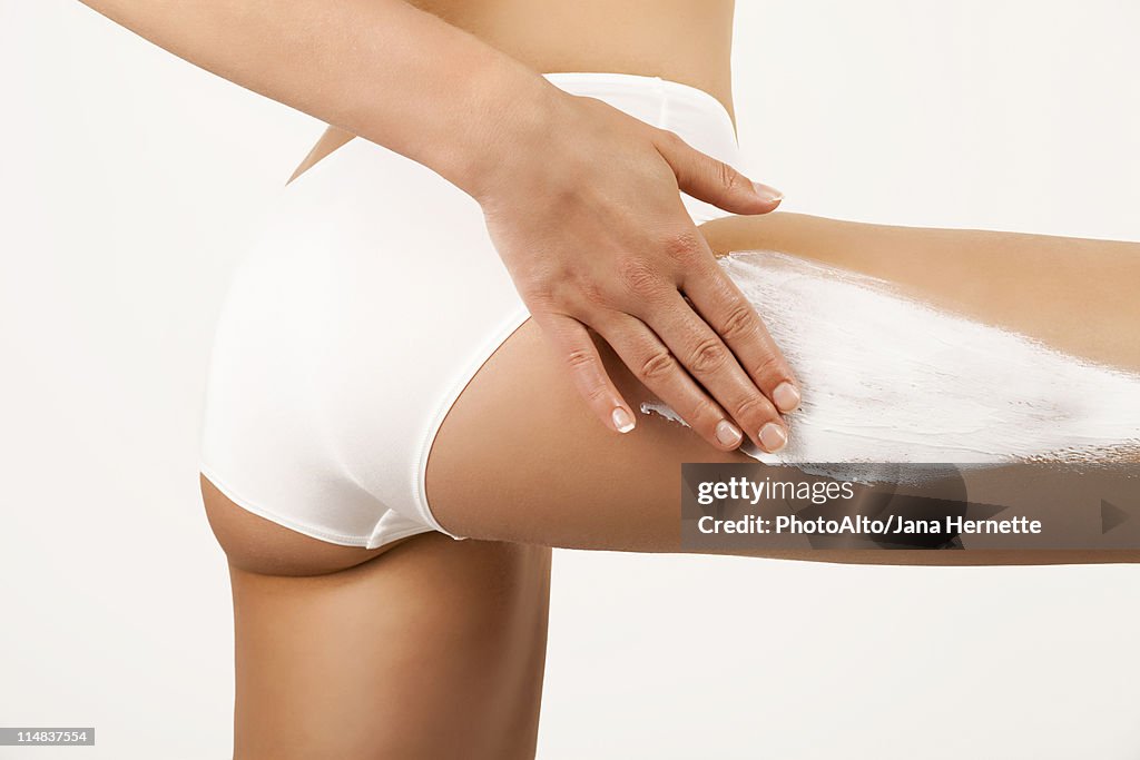 Woman applying moisturizer to thigh, cropped