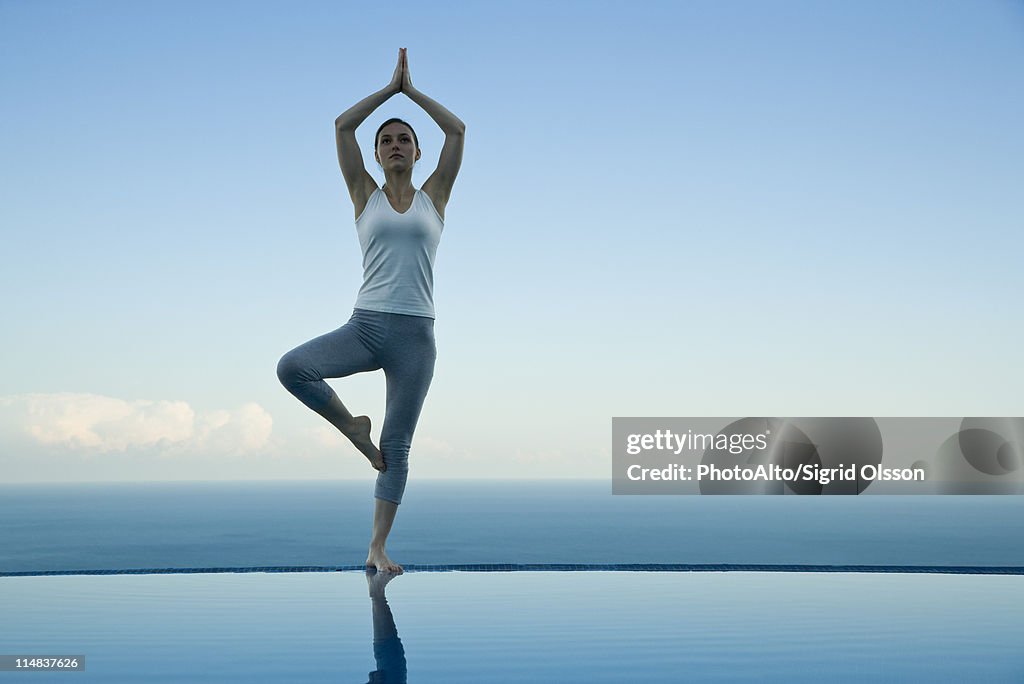 Woman standing in tree pose on edge of infinity pool