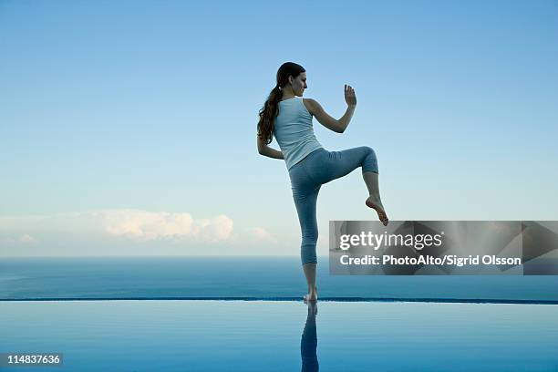 woman practicing tai chi chuan on edge of infinity pool - tai chi imagens e fotografias de stock