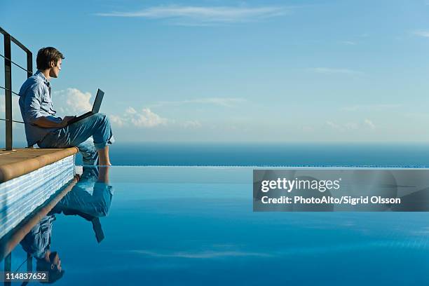 man sitting at edge of infinity pool with laptop computer, looking at view - water reflection stock pictures, royalty-free photos & images